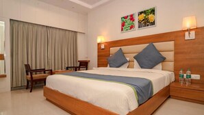 A hotel room with a large bed, a desk, two chairs, a wooden headboard, and two wall-mounted lamps. - HOTEL BLUE ORCHID GROUP OF MR HOTELS (Udaipur)