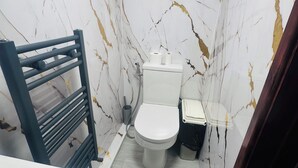 Kylpyhuone, jossa on wc, pieni roskakori ja pyyheteline.
