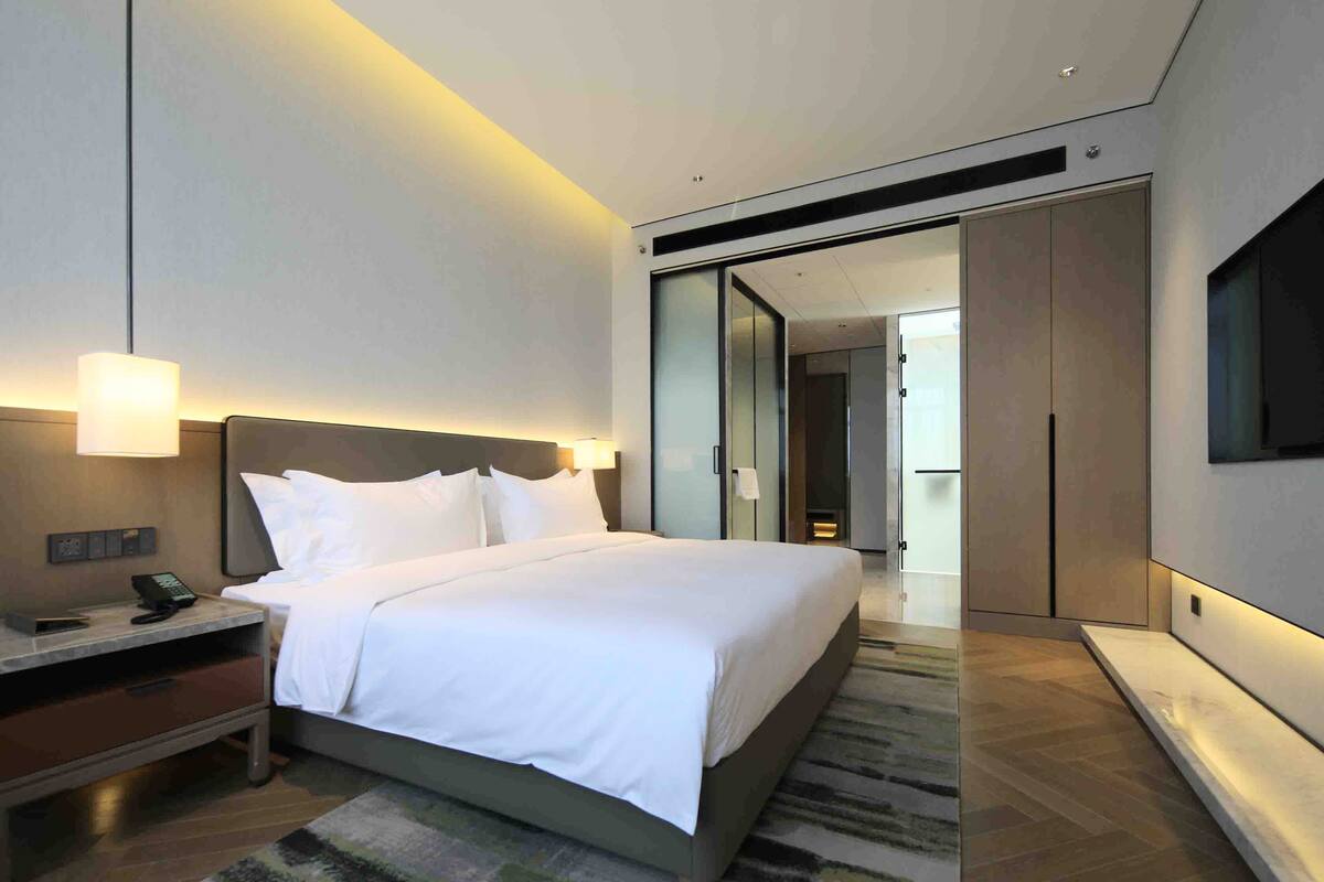 Una habitación de hotel moderna con cama, mesita de noche, lámpara y televisor montado en la pared.