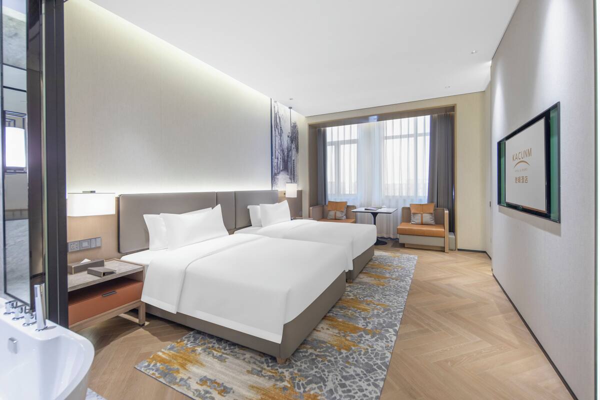 Una habitación de hotel moderna con dos camas, un ventanal amplio, un escritorio y un baño.