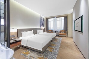 Una habitación de hotel moderna con dos camas, un ventanal amplio, un escritorio y un baño.