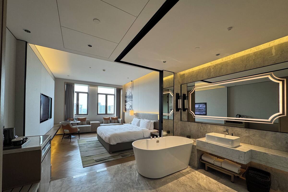 Una habitación de hotel moderna con una cama grande, una zona de estar, una bañera y un espejo amplio.