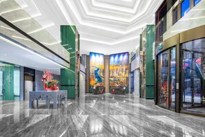 Un moderno vestíbulo de hotel con piso de mármol, paredes de acento verde y un gran mural con vistas a la ciudad.