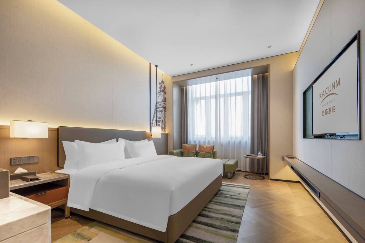 Una habitación de hotel con una cama grande, un escritorio, una silla, un televisor y una ventana con cortinas.