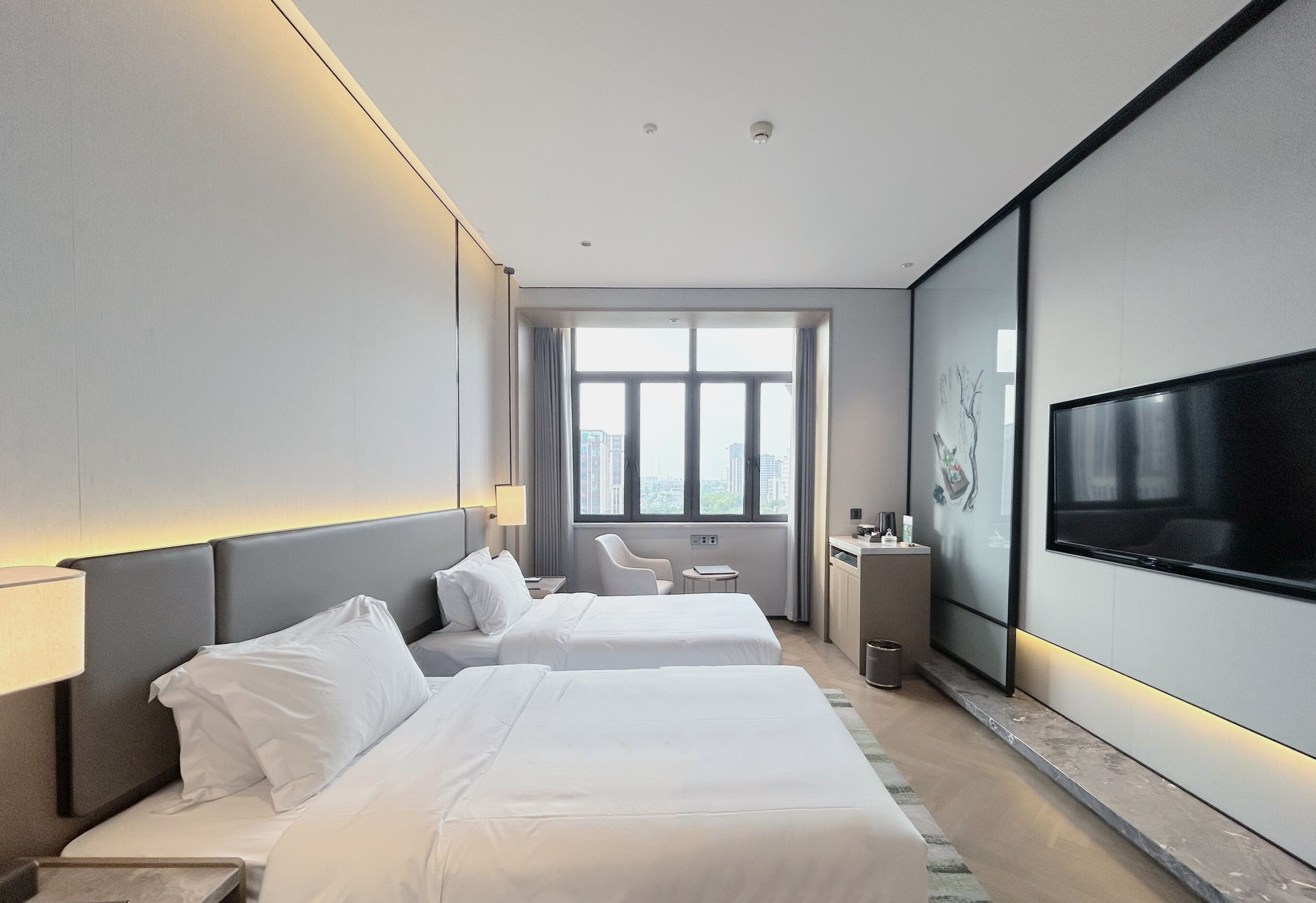 Una habitación de hotel moderna con dos camas, televisión, escritorio y vistas a la ciudad.
