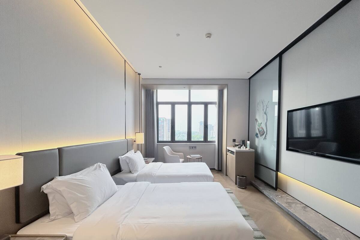 Una habitación de hotel moderna con dos camas, televisión, escritorio y vistas a la ciudad.