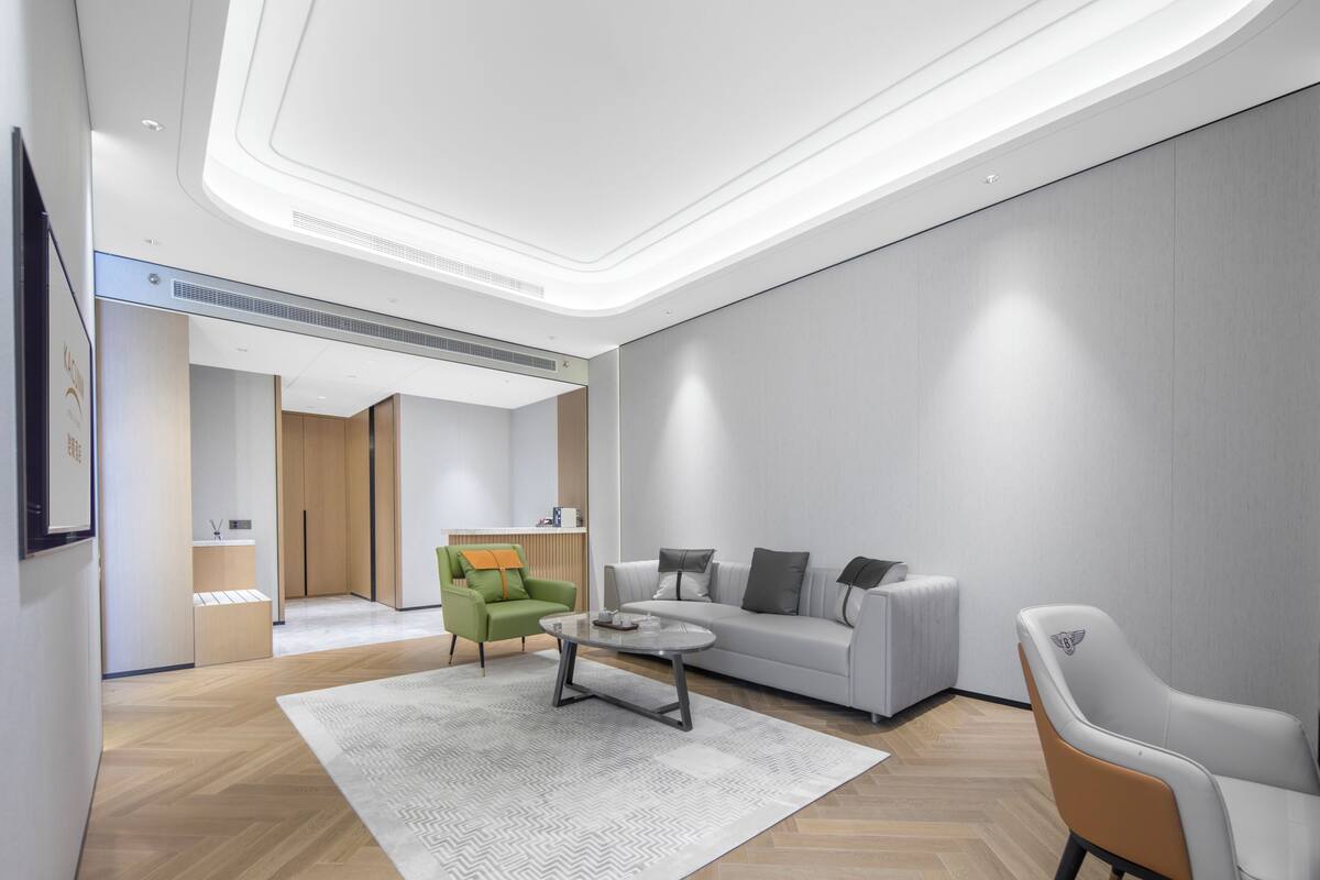 Una sala moderna con un sofá, un sillón verde, una mesa de centro redonda y un sillón blanco.