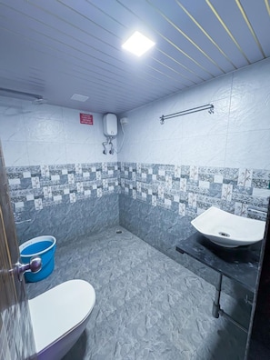 Un baño con dos lavamanos, un inodoro, una ducha y un cubo azul.