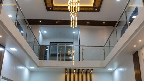 Un vestíbulo espacioso con techo alto, un candelabro central, una zona de estar con sofás y sillones, y una barandilla de cristal con vistas al nivel inferior.