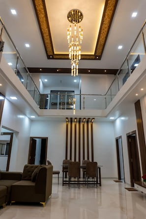 Un vestíbulo espacioso con techo alto, un candelabro central, una zona de estar con sofás y sillones, y una barandilla de cristal con vistas al nivel inferior.