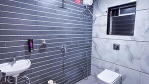 Un baño con lavamanos, inodoro y bidé, con paredes de azulejos oscuros y suelo de mármol.