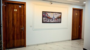 A hallway with three wooden doors, a marble floor, and a painting of a Parisian street scene. - Millennium Suites (Gurugram)