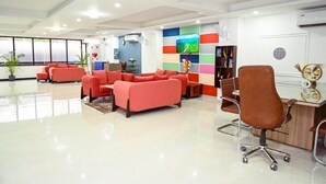 A modern office space with red sofas, a brown office chair, a wooden desk, and a colorful wall with a TV. - Millennium Suites (Gurugram)