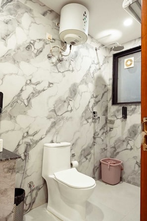 A bathroom with a toilet, a shower, and a marble wall. - Millennium Suites (Gurugram)