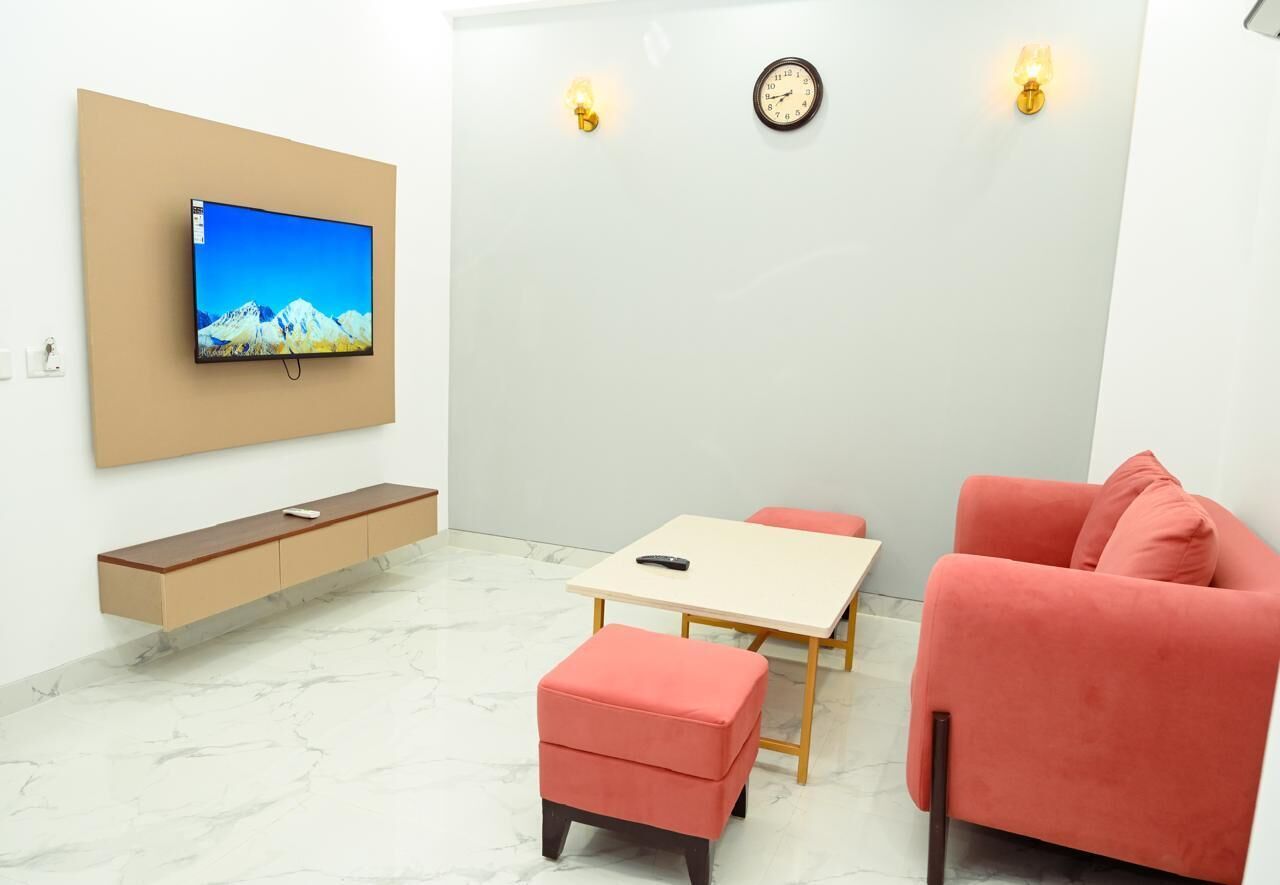 A living room with a TV, a sofa, a table, and a clock on the wall.