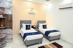 Habitación de hotel con dos camas, suelo de mármol, aire acondicionado instalado en la pared y un cuadro con una vista urbana enmarcada.