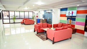A modern lobby with red sofas, a coffee table, and a TV on the wall. - Millennium Suites (Gurugram)