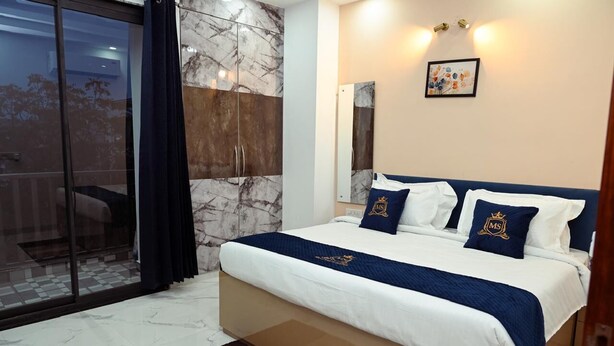 A bedroom with a large bed, a sliding glass door, a marble wall, and a framed picture on the wall. - Millennium Suites (Gurugram)