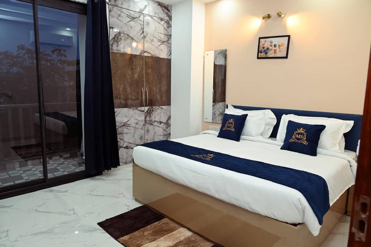 A bedroom with a large bed, a sliding glass door, a marble wall, and a framed picture on the wall.