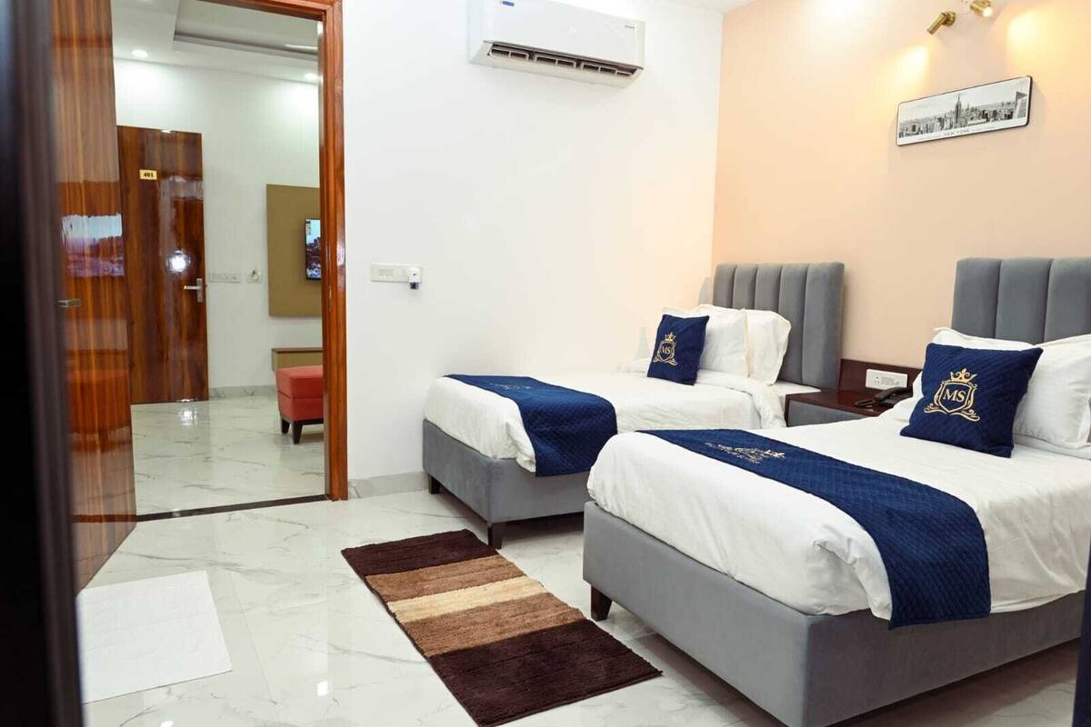 A hotel room with two beds, a marble floor, an air conditioning unit, and a cityscape picture on the wall.
