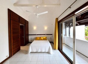 Ein Schlafzimmer mit Bett, Deckenventilator, Schiebetür und Blick auf Grünfläche.