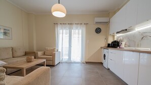 Una sala de estar moderna con un sofá, una mesa de centro y una mesa de comedor. Cuenta con una zona de cocina con lavadora y fregadero.