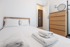 Ein ordentlich bezogenes Bett mit weißen Leinentüchern, einem Holz-Kopfteil und einer Reihe Handtüchern auf dem Bett.