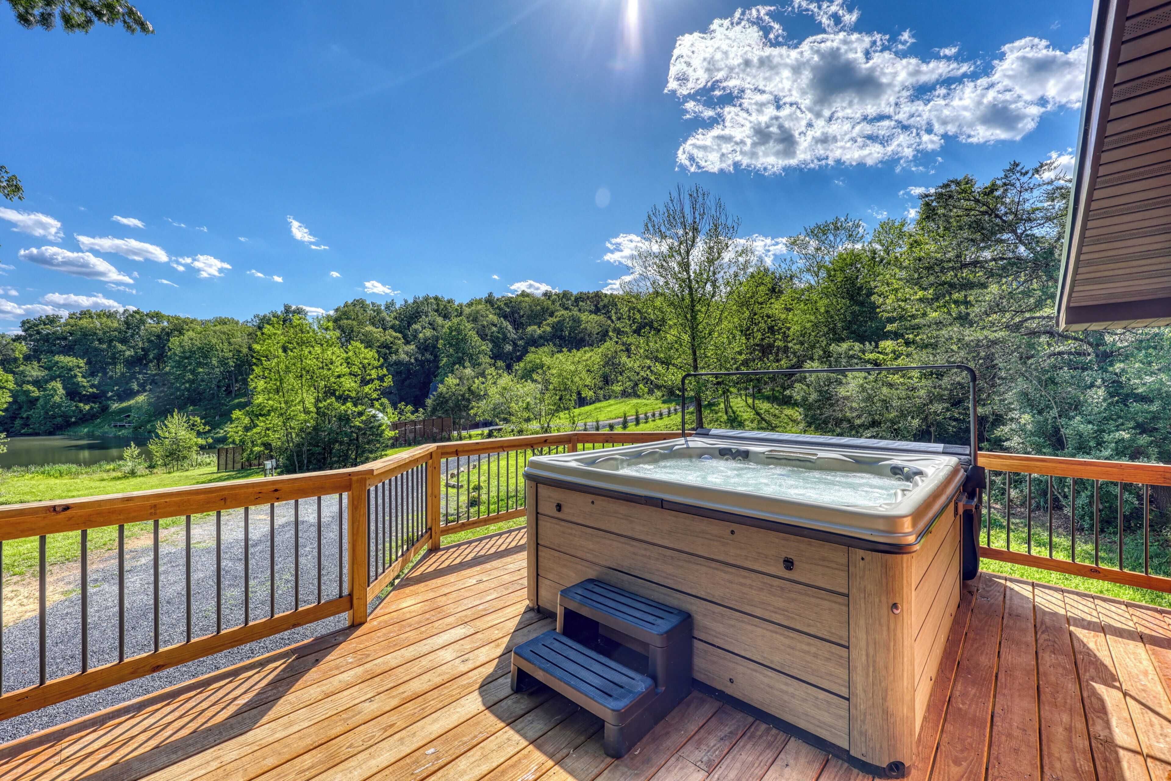 A hot tub on a wooden deck with a view of a lake and forest.