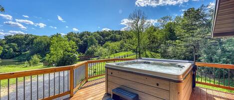 A hot tub on a wooden deck with a view of a lake and forest.