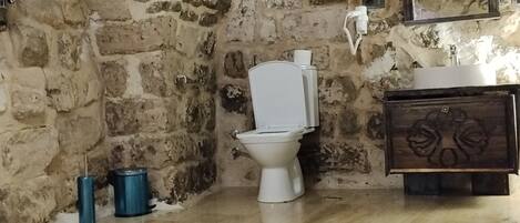 Et badeværelse med en stenbue, et hvidt toilet, et træskab og en vask.