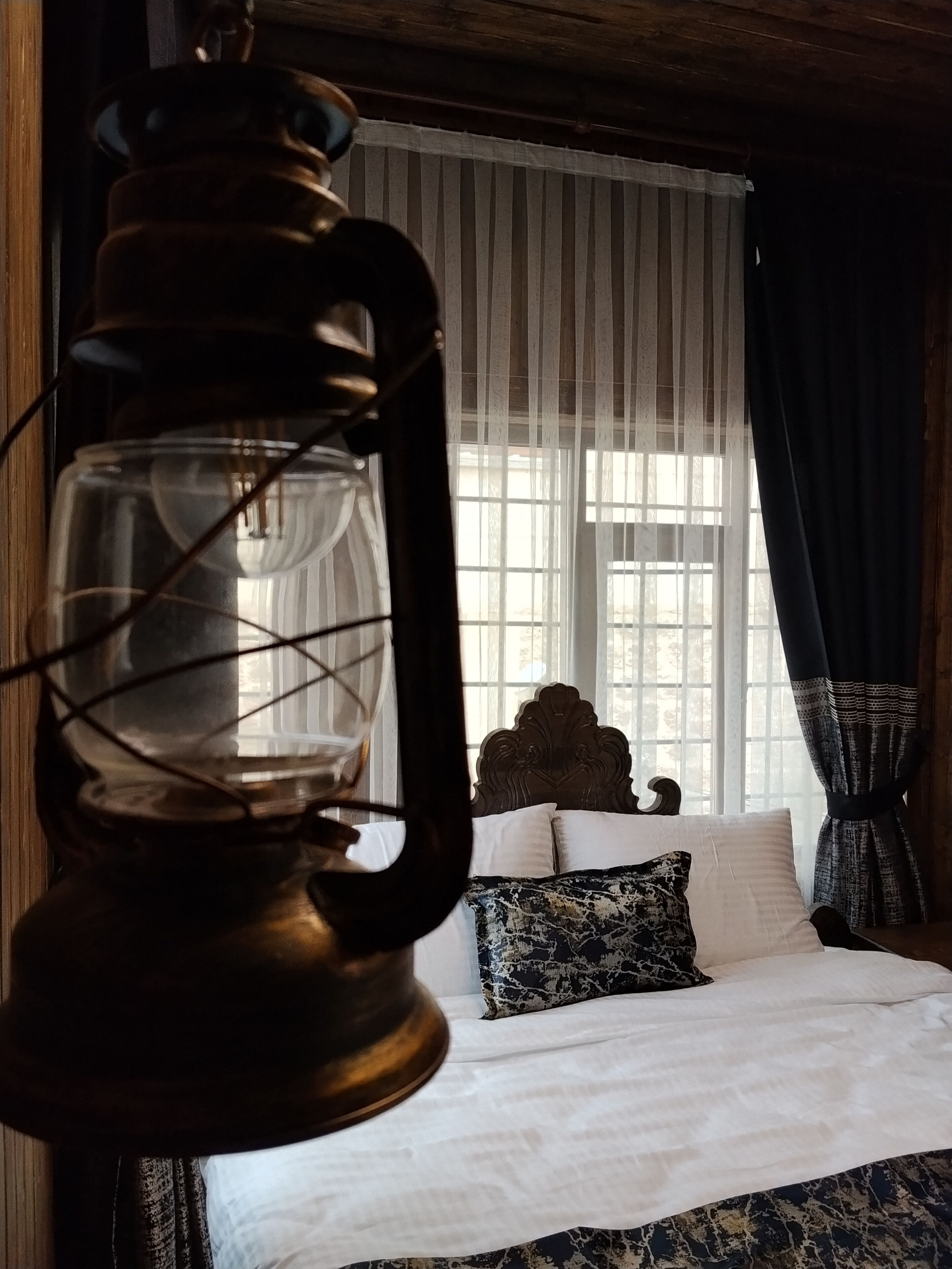 Une chambre avec un lit, une tête de lit en bois, une lanterne suspendue et des rideaux en voile.
