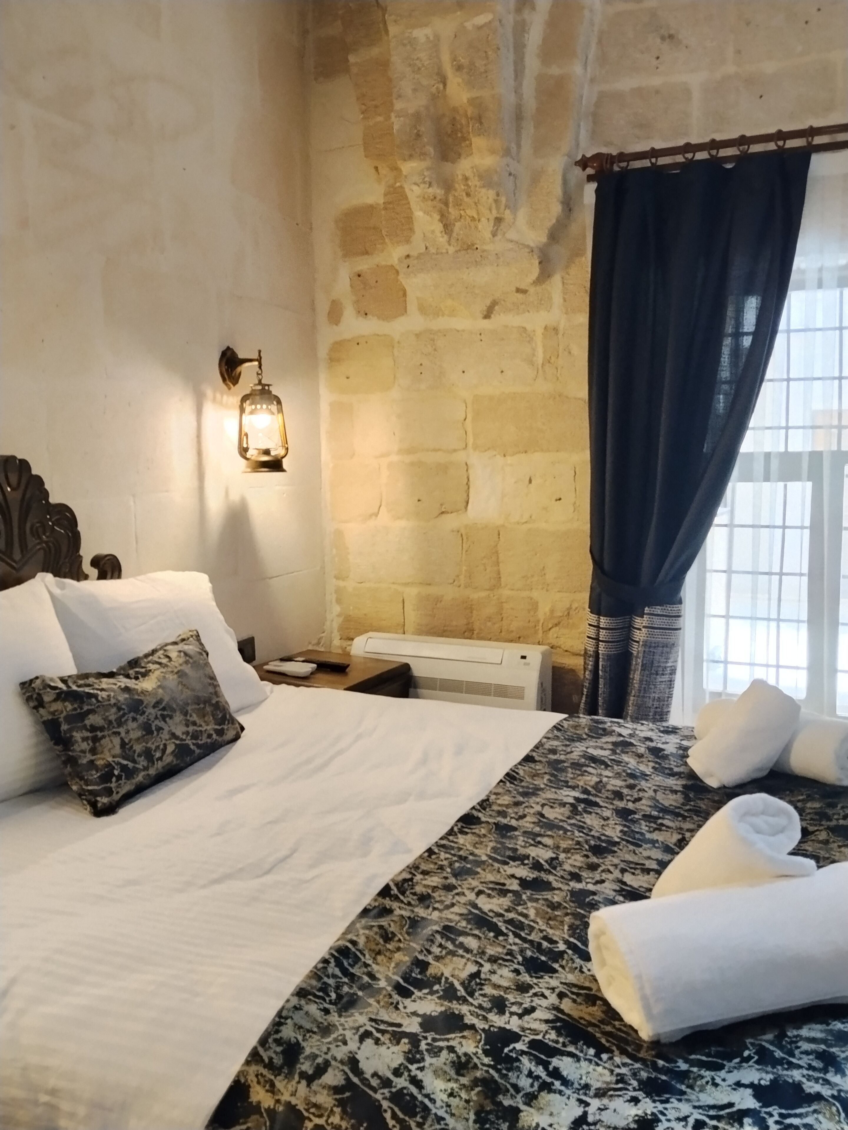 A room with a bed, a wall-mounted light, a window with curtains, and a radiator.