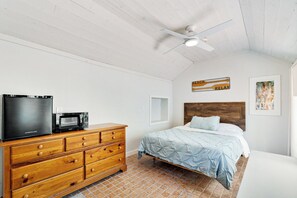Een slaapkamer met een bed, een houten dressoir, een plafondventilator en een wanddecoratie.