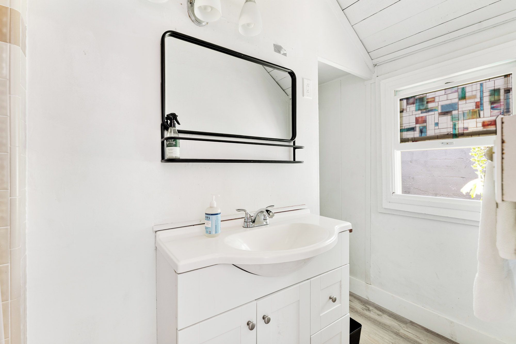 A bathroom with a white vanity, a mirror, and a window with a view of a building.