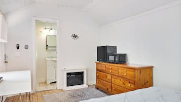 A bedroom with a bed, a wooden dresser, a white desk, and a small fireplace.