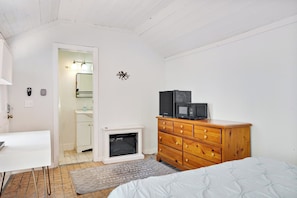 Un dormitorio con una cama, un aparador de madera, un escritorio blanco y una pequeña chimenea.