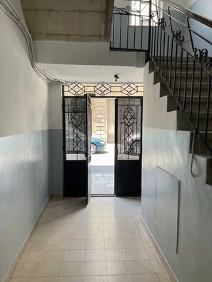 Ein schmaler Flur mit Treppe auf der rechten Seite, die zu einer Tür mit geometrischem Muster führt.
