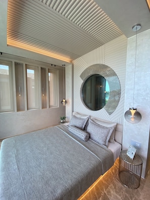 A modern bedroom with a large bed, a round mirror, and a small side table.