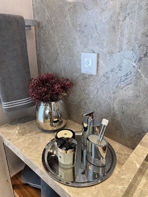 A bathroom vanity with a marble countertop, a towel, a vase with dried flowers, and toiletries.