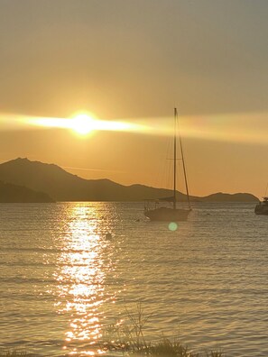 A sunset over a calm sea with a sailboat and distant mountains.