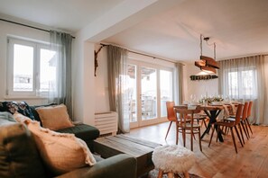 Un salon moderne avec un canapé, une table à manger dressée pour six personnes et une porte-fenêtre coulissante donnant sur un espace extérieur.
