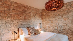 A bedroom with stone walls, a bed with patterned pillows, a bedside lamp, and a woven light fixture. - Istrian Villa Beatrice Near Pula (Vodnjan)