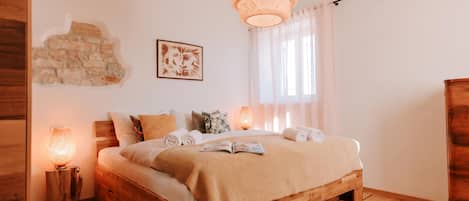 A wooden bed with a beige blanket, a stone wall, a framed picture, and a hanging light fixture.