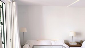 Ett minimalistiskt hotellrum med en säng, ett nattduksbord, en lampa och en korg av rotting med diverse föremål på golvet.