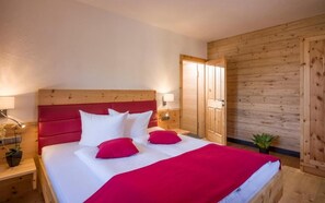 A bedroom with a wooden headboard, a bed with white and red bedding, a nightstand with a lamp, and a wooden wardrobe. - Refugium Dolomiten & Chalet (Sillian)