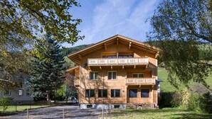 A multi-story wooden building with balconies, surrounded by trees and a grassy area. - Refugium Dolomiten & Chalet (Sillian)