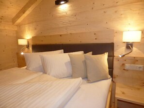 A wooden cabin-style room with a bed, headboard, wall-mounted lamps, and a wooden ceiling. - Refugium Dolomiten & Chalet (Sillian)