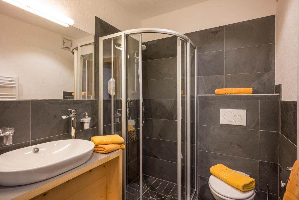 Ein Badezimmer mit einem weißen Waschbecken, einer Duschkabine aus Glas und einer Toilette mit einem gelben Handtuch.
