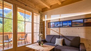 A wooden interior with a sofa, a table with a bottle, and a view through large windows. - Refugium Dolomiten & Chalet (Sillian)