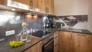A modern kitchen with wooden cabinets, a black countertop, and a stainless steel backsplash. - Refugium Dolomiten & Chalet (Sillian)